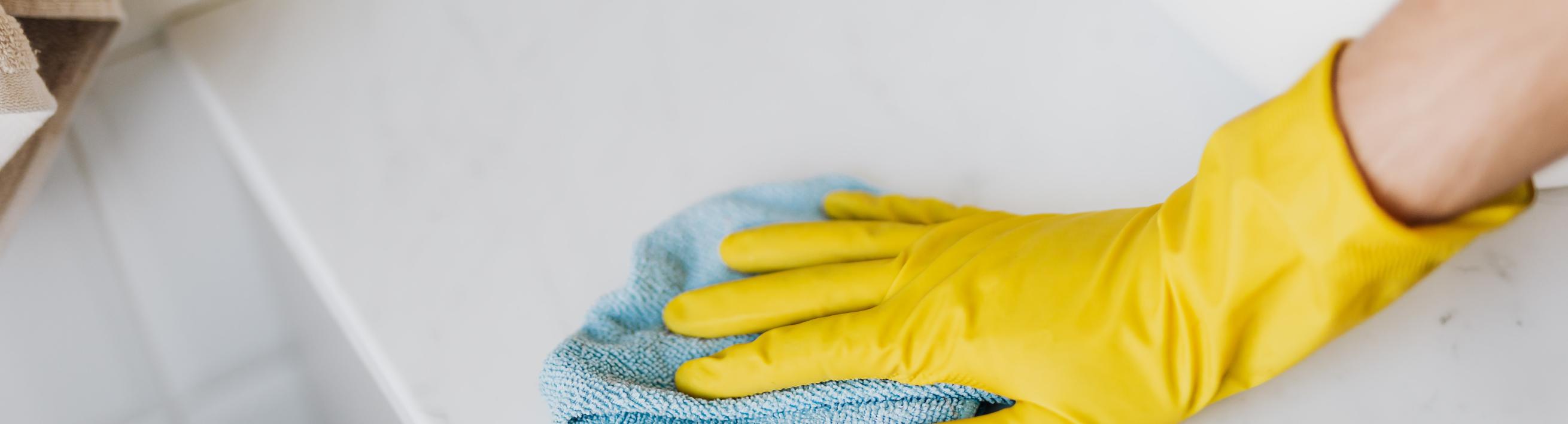A gloved hand using a rag to clean a white surface.