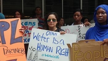 Diverse crowd of protesters holding up signs - center sign reads: Clean Water is a Human Right #Waterislife