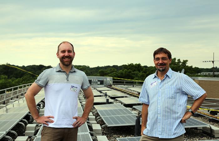 Jason Bing (left) and Charles Griffith (right) standing atop Miller Manor, Ann Arbor Affordable Housing, in front of their solar power display