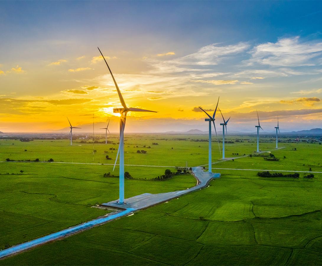 A diptych: the first image features a close-up shot of solar panels on a rooftop set against a backdrop of trees and a city skyline, the second image features wind turbines in a bright grassy field.
