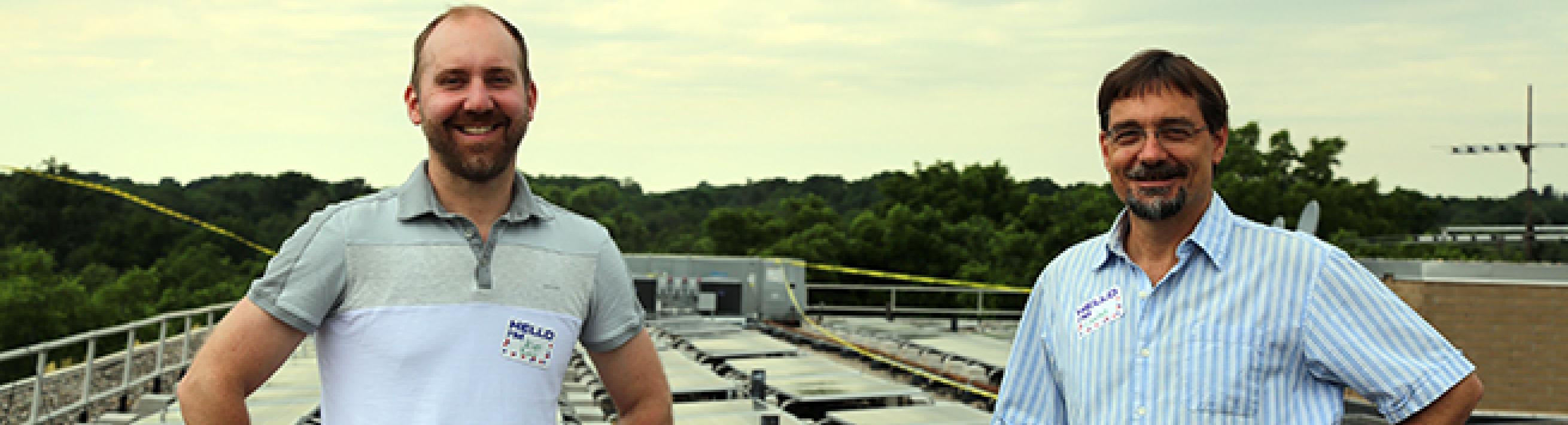 Jason Bing (left) and Charles Griffith (right) standing atop Miller Manor, Ann Arbor Affordable Housing, in front of their solar power display