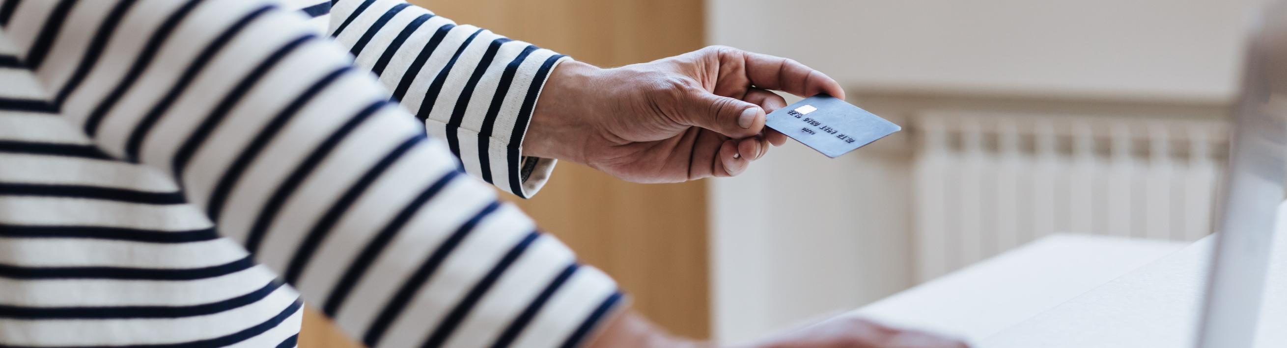 A person typing on a laptop with one hand and holding a credit card with the other