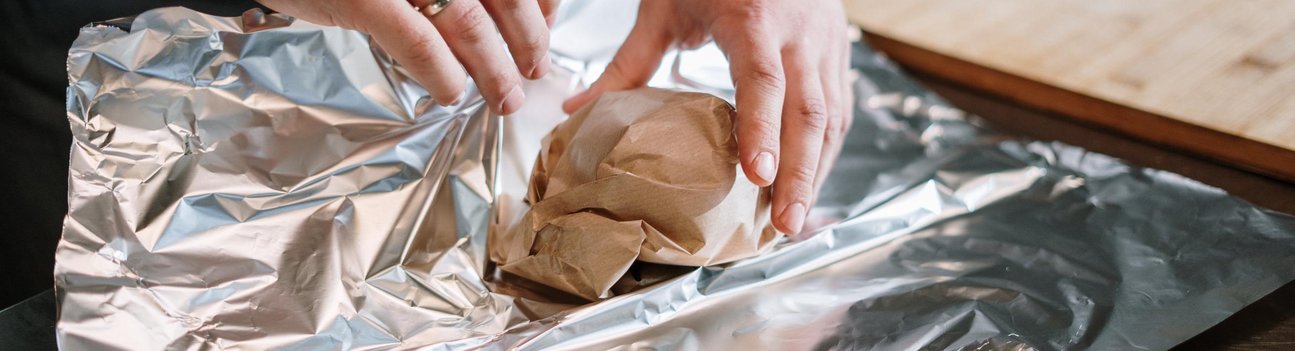 A person wrapping food in paper and foil.