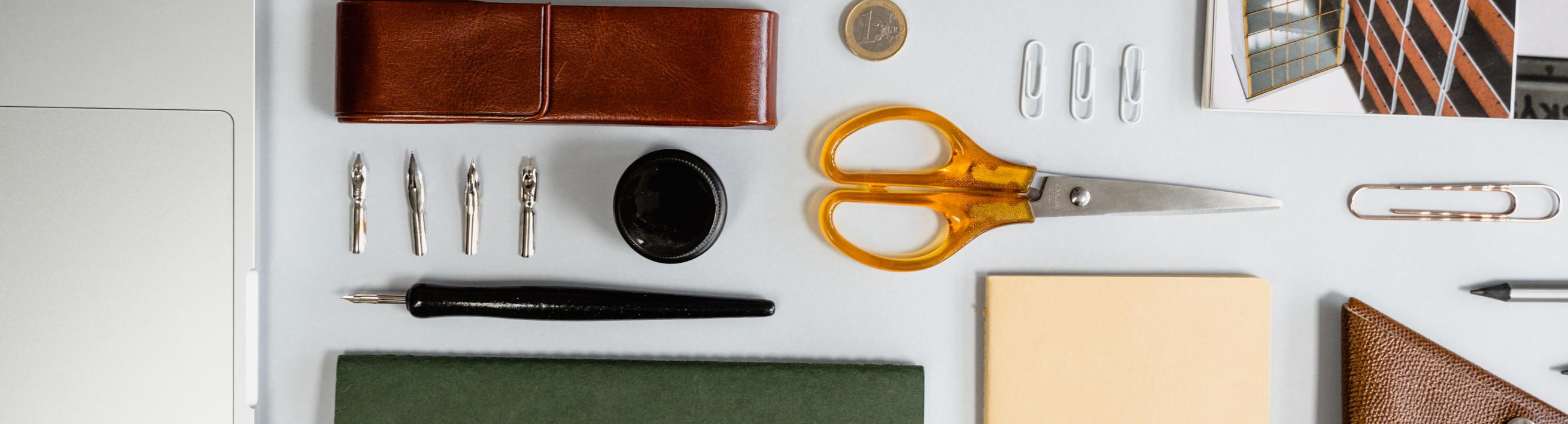 A collection of office supplies including a pen, notepads, scissors, and a paperclip.