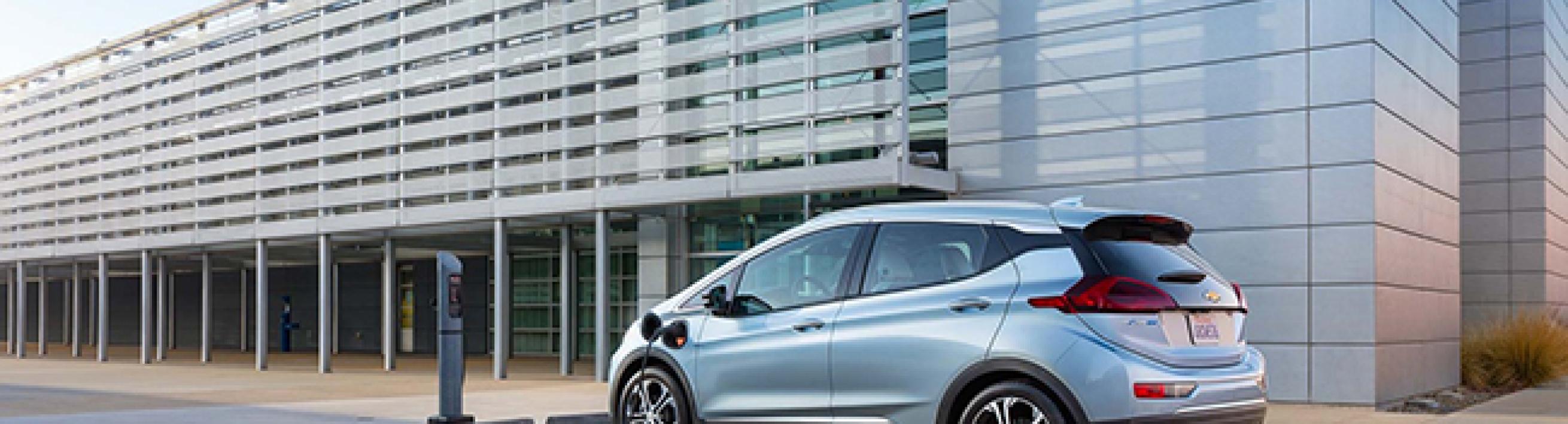 A silver Chevrolet Bolt sits in front of a shiny mirrored building. 