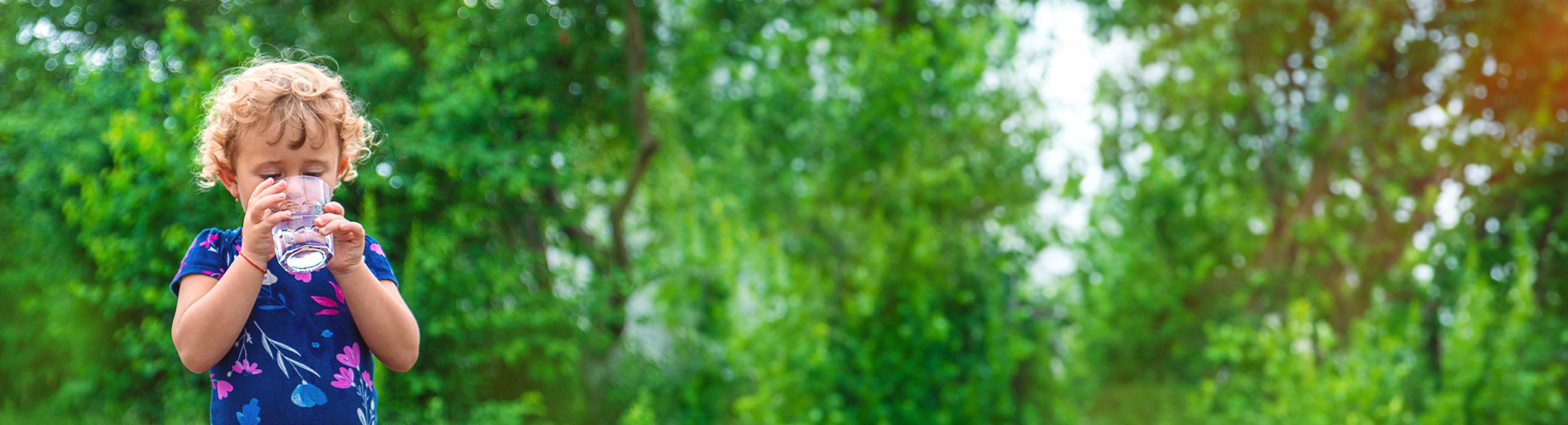 Child drinking clean water with green trees in background