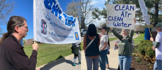 Left: Gus is holding up a large Save the EPA Banner. Right: Carla, another member of Ann Arbor Indivisible, holding up a Clean Air & Clean Water sign